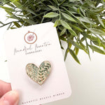 A hand holding a 'botanical heart' magnetic needle minder