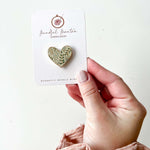 A hand holding a magnetic needle minder with a botanical heart design
