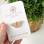 A hand holding the Butterfly Magnetic Needle Minder