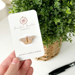 A hand holding the Butterfly Magnetic Needle Minder in front of a plant