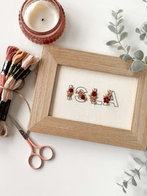 Mini Floral Alphabet Embroidery Pattern featuring the name 'ISLA' on fabric with embroidery supplies.