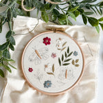 Embroidery hoop with floral and butterfly design on a white fabric background with green leaves.