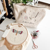 Embroidery hoop with butterfly design and project bag on a table.