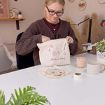A woman, sat in a studio, pulling craft supplies out of her embroidery project bag