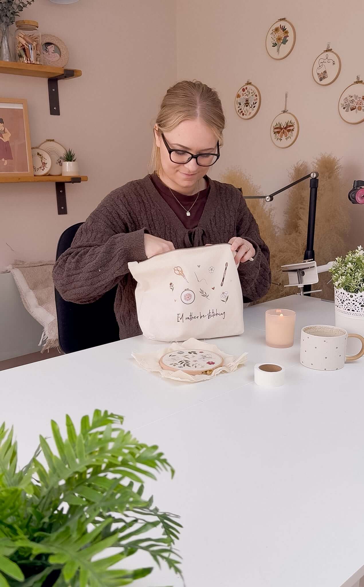 A woman, sat in a studio, pulling craft supplies out of her embroidery project bag