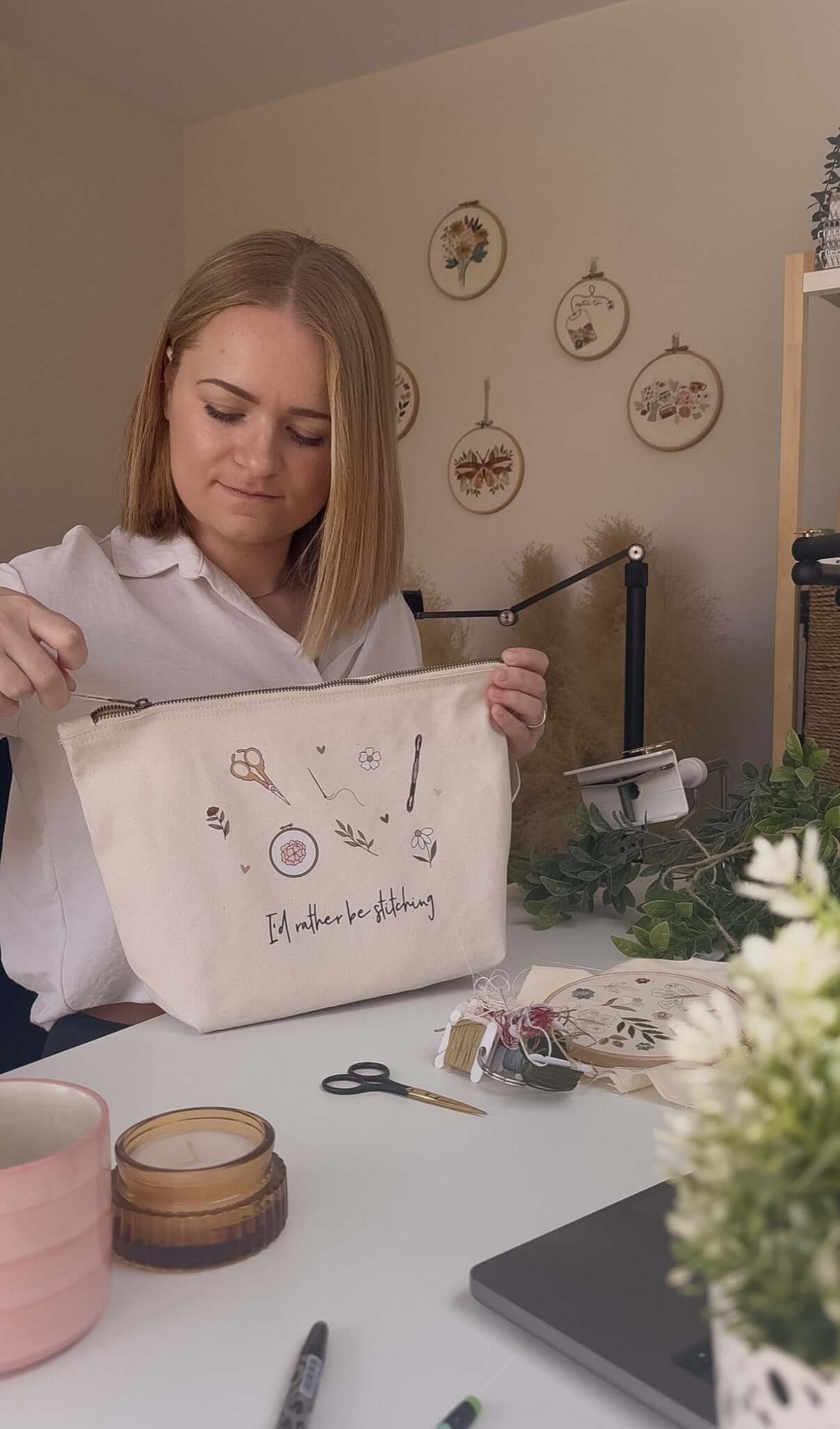 Woman holding a project bag with embroidery designs on a table with crafting supplies.