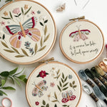 Three embroidered hoops with butterfly patterns on a white surface with embroidery threads and scissors.