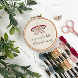 Butterfly embroidery pattern with floral design and motivational quote, surrounded by embroidery threads and scissors on a white background.