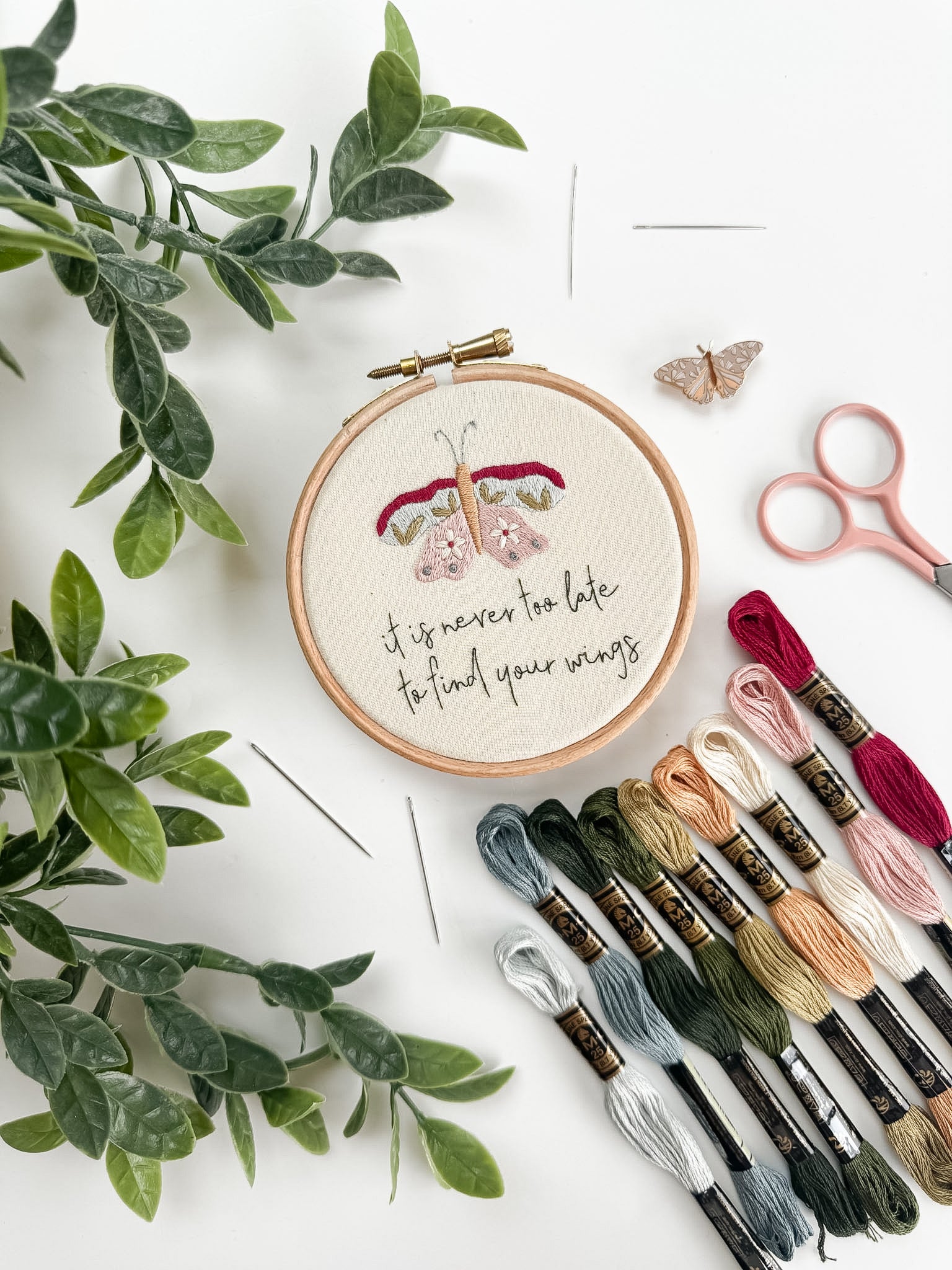 Butterfly embroidery pattern with floral design and motivational quote, surrounded by embroidery threads and scissors on a white background.
