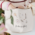 Person holding a white project bag with embroidery designs and 'I'd rather be stitching' text on a light background.