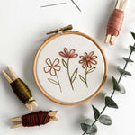 Beginner Embroidery Kit showing a floral design in a hoop with colorful threads and clothespins.