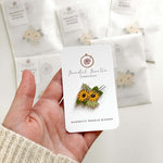 Magnetic Needle Minder featuring sunflowers, held in hand with packaging in background, perfect for needlework projects.